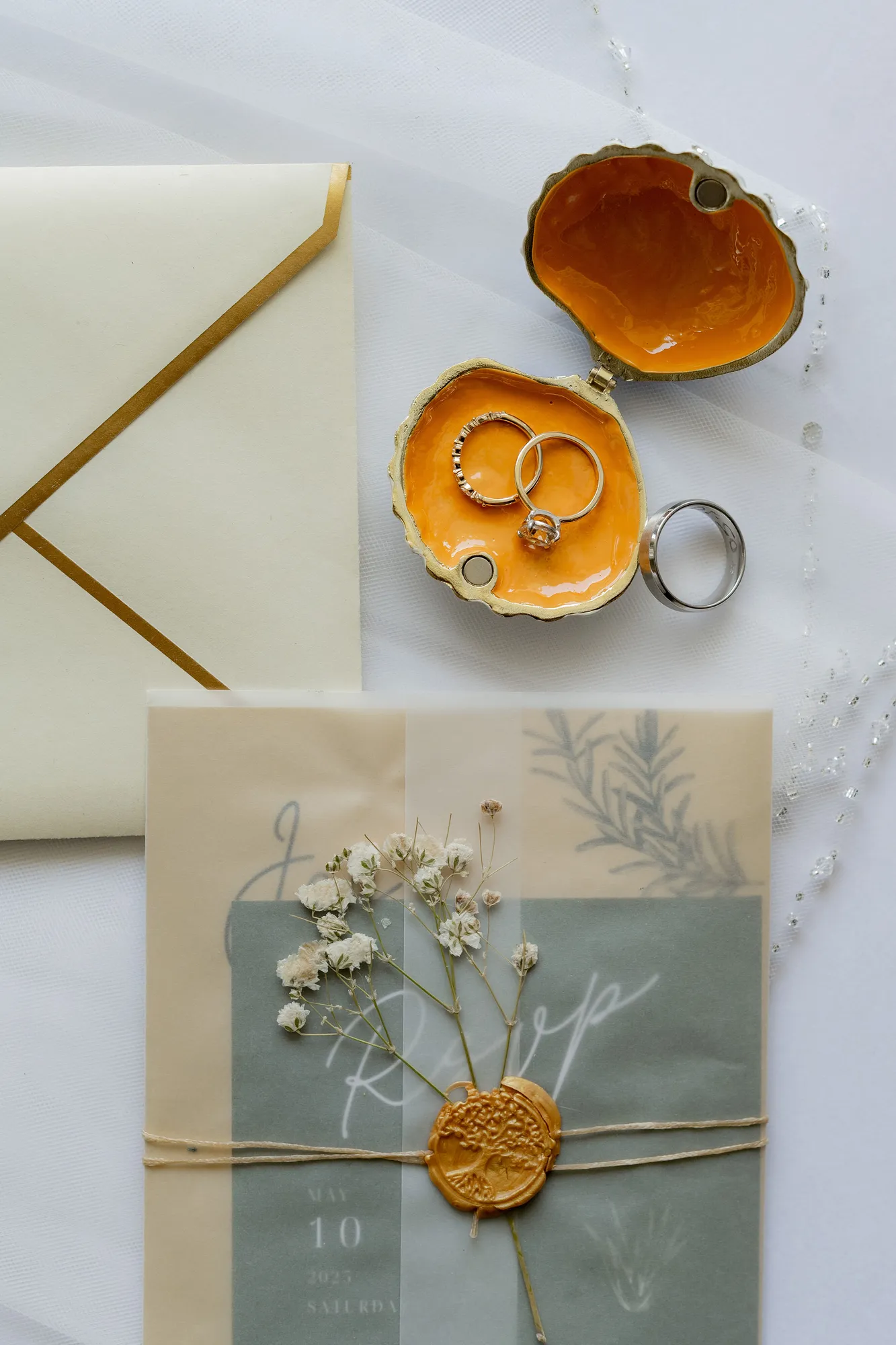 Wedding rings, a vellum invitation with a wax seal, and baby's breath styled as a flat-lay