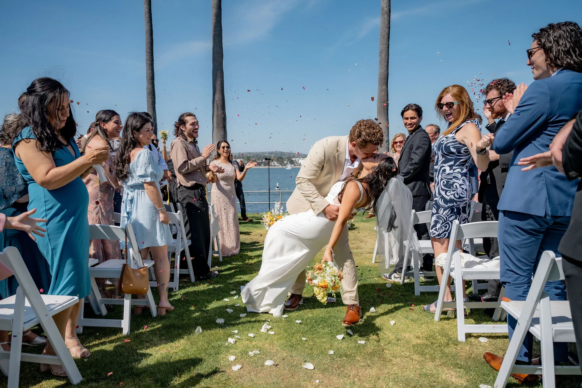 Guests toss petals as the newlyweds kiss during their wedding recessional