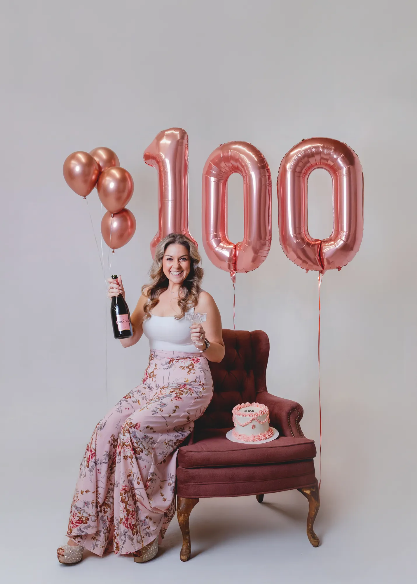Jen Klaus seated with champagne and a pink 100 cake at her milestone celebration